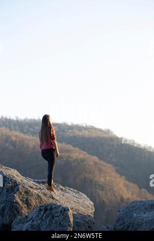 Una giovane donna gode della vista dalla cima della montagna. Panorama della catena montuosa illuminata dai raggi del sole Foto Stock