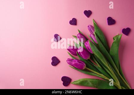 Bouquet di tulipani viola con cuori su sfondo rosa. Festa della mamma, giorno di San Valentino, festa di compleanno. Biglietto d'auguri. Copia spazio, in alto vie Foto Stock