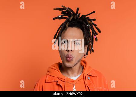 ritratto di uomo multirazziale trafitto con orsacchiette che infilano le labbra isolate su sfondo corallo Foto Stock