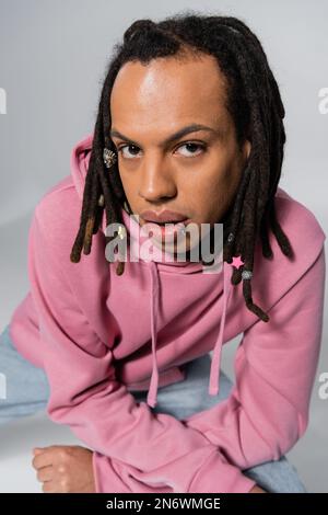 vista dall'alto di un uomo multirazziale e trafitto con dreadlocks che guarda la macchina fotografica sul grigio Foto Stock