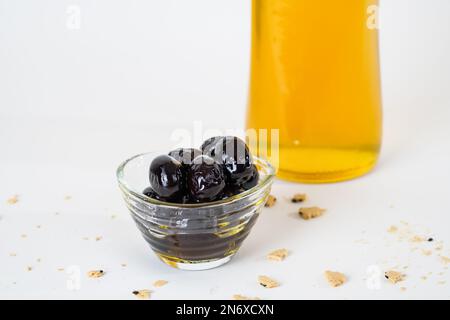 Vista ravvicinata della bottiglia di vetro di olio d'oliva e delle olive nere in salamoia isolate su sfondo bianco. Foto Stock