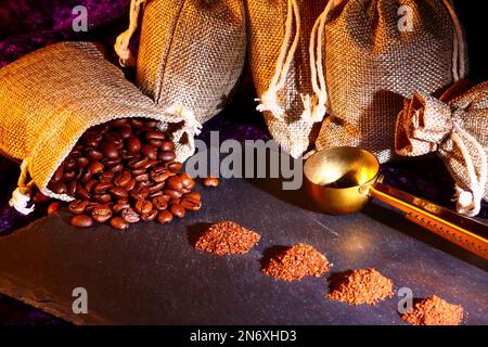 Sacchi di Hessian pieni di chicchi di caffè torrefatto con mucchi di caffè appena macinato Foto Stock
