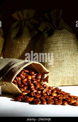 Sacchi di Hessian pieni di chicchi di caffè arrostiti che fuoriescono da un sacco aperto Foto Stock