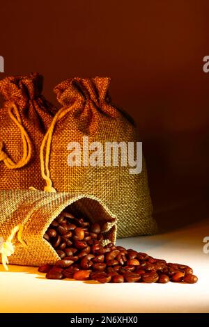 Sacchi di Hessian pieni di chicchi di caffè arrostiti che fuoriescono da un sacco aperto Foto Stock