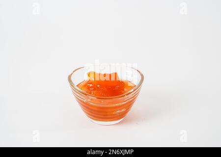 Marmellata di pesche fatta in casa in una piccola ciotola di vetro isolata su fondo bianco. Foto Stock