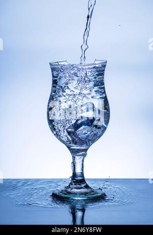 L'immagine di versare acqua potabile, in un vetro rotto, che fa sentire rinfrescato su sfondo bianco sfocato, spruzzi d'acqua, acqua frizzante, Foto Stock