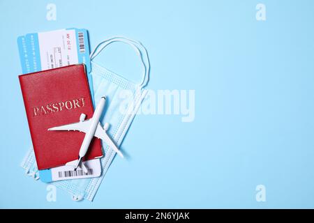 Composizione piatta con passaporto, maschera protettiva e piano giocattolo su sfondo azzurro. Spazio per il testo Foto Stock