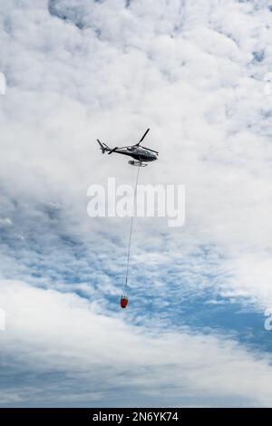 Wendefurth, Germania - 17.06.22: Un elicottero con un serbatoio pieno di acqua estinguente vola verso un incendio boschivo Foto Stock