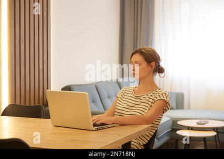 Giovane donna che lavora, legge o studia sul suo laptop nell'appartamento. Imprenditore professionista remoto lavorare con il laptop in appartamento moderno Foto Stock