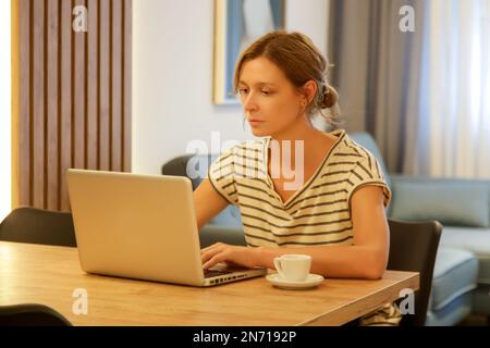 Giovane donna che lavora, legge o studia sul suo laptop nell'appartamento. Imprenditore professionista remoto lavorare con il laptop in appartamento moderno Foto Stock