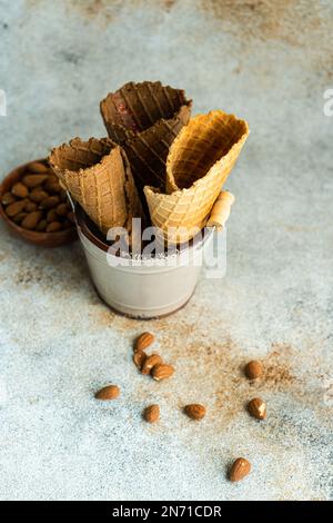 Metallo bucato riempito con tre coni di waffle vuoti accanto a una ciotola di mandorle Foto Stock