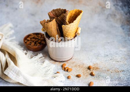 Secchio di metallo riempito con tre coni di waffle vuoti vicino a una ciotola di mandorle Foto Stock