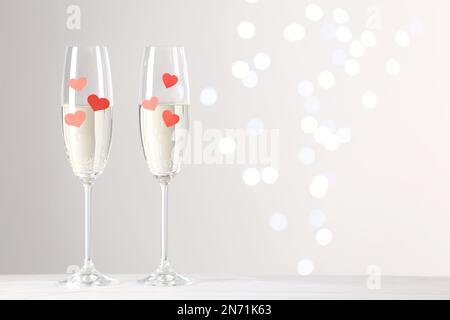 Bicchieri di champagne con cuori di carta su un tavolo bianco contro luci sfocate. Spazio per il testo Foto Stock