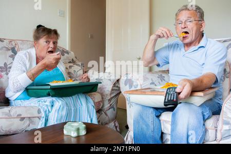 Pensione: Cena TV. Una coppia anziana si è impegnata più con la televisione che l'una con l'altra. Da una serie di immagini correlate. Foto Stock