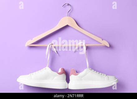 Sneaker eleganti con lacci bianchi appesi su un appendiabiti in legno su sfondo viola Foto Stock