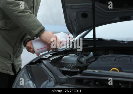 Uomo che riempie il radiatore dell'automobile con antigelo all'aperto, primo piano Foto Stock