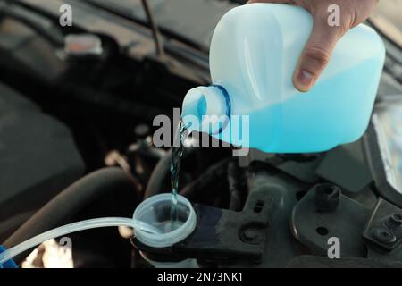 Man che versa l'antigelo dal contenitore in plastica nel serbatoio del liquido lavacristalli, fare un primo piano Foto Stock