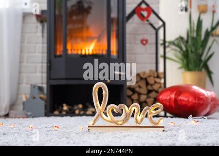 Decorazioni di San Valentino vicino a stufa con camino e legna da ardere. Accogliente casa cuore in interni con vaso piani, giorno di San Valentino in famiglia amore nido. Foto Stock