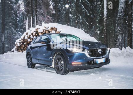 Italia, Veneto, Belluno, a Mazda Motor Corp CX-30 veicolo di servizio sportivo crossover (SUV) su una strada di montagna in inverno durante una nevicata, Dolomiti Foto Stock