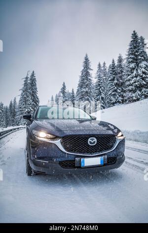 Italia, Veneto, Belluno, a Mazda Motor Corp CX-30 veicolo di servizio sportivo crossover (SUV) su una strada di montagna in inverno durante una nevicata, Dolomiti Foto Stock