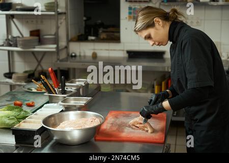 Lo chef donna taglia il filetto di pollo crudo su un tagliere Foto Stock