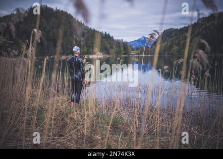 Triatleta professionista prima di nuotare, allenarsi in un lago di montagna limpido a Allgäu, Alatsee, Baviera, Germania Foto Stock