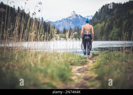 Triatleta professionista prima di nuotare, allenarsi in un lago di montagna limpido a Allgäu, Alatsee, Baviera, Germania Foto Stock