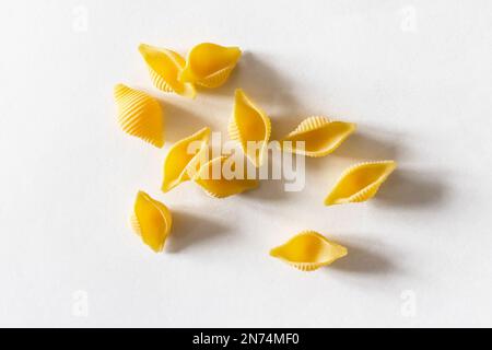 vista dall'alto di diversi pezzi di pasta rigata conchiglie non cotti a secco in primo piano su carta bianca Foto Stock