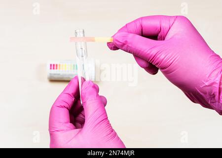 mani che tengono la carta di litmus acido rosa e la provetta su un tavolo leggero Foto Stock