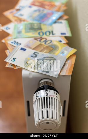 Molte bollette in euro si trovano sul radiatore, il termostato del radiatore con livello di impostazione 3 circa 2ö°C., l'immagine simbolo, il tasso di risparmio energetico, i costi energetici, i costi di riscaldamento in aumento, Foto Stock