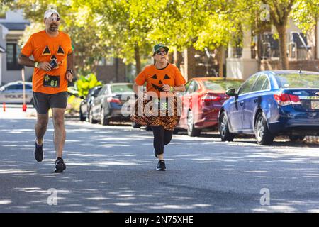 Suwanee, GA / USA - 15 ottobre 2022: Una coppia che indossa le camicie di zucca corre lungo una strada residenziale mentre si avvicina al traguardo di una gara 5K. Foto Stock