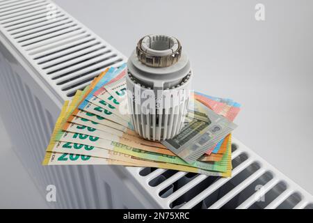 Termostato di riscaldamento, bollette euro sul radiatore, sfondo bianco, immagine simbolo, sostituire il termostato di riscaldamento, sostituire il termostato, risparmiare sui costi energetici, Foto Stock
