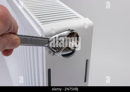 La mano dell'uomo con una chiave a forcella rotante allenta l'inserto della valvola del radiatore sul radiatore, sfondo bianco, immagine simbolo, inserto della valvola di ricambio, difettoso, Foto Stock