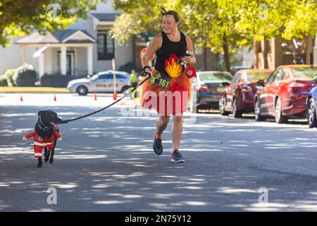 Suwanee, GA / USA - 15 ottobre 2022: Una donna vestita come fuoco corre con il suo cane, vestita come un vigile del fuoco, negli spiriti Spooky 5K, il 15 ottobre 2022. Foto Stock