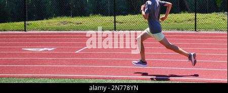 Vista laterale di un corridore di scuola superiore maschio che corre veloce sulla curva di una pista all'aperto. Foto Stock