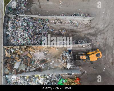 Processo di movimentazione di una pila di rifiuti con attrezzature pesanti, pala gommata in discarica, vista dall'alto aerea. Concetto di smaltimento e trasferimento dei rifiuti. Foto Stock