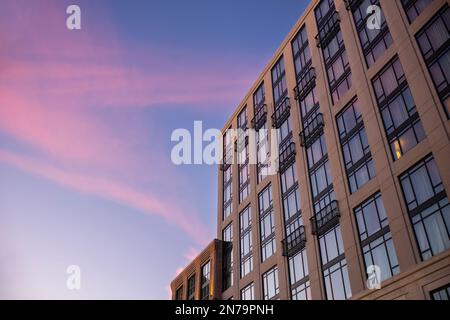 La facciata di un edificio con una stanza illuminata da una lampada da tavolo, fotografata al tramonto con un retrogusto delle nuvole sopra nel cielo. Foto Stock