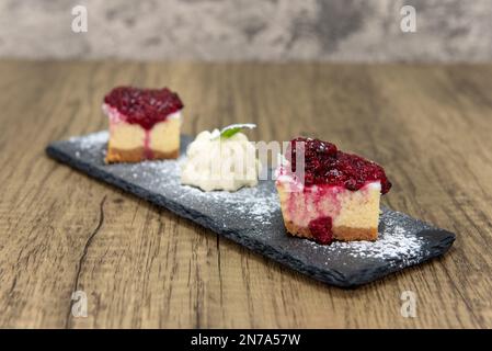Delizioso dessert di cheesecake condito con condimento di frutta e servito con panna montata. Foto Stock