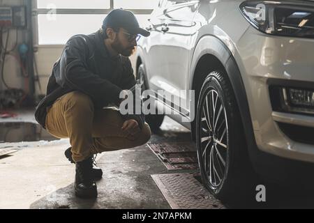 un meccanico che controlla la geometria e la sospensione di una ruota di un'automobile usando gli attrezzi, colpo pieno. Foto di alta qualità Foto Stock