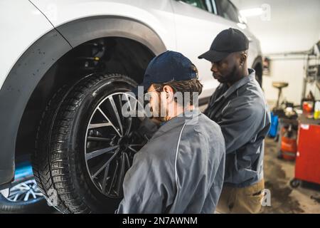 scatto posteriore medio di due meccanici che cambiano la ruota su un'automobile, officina di riparazione dell'automobile. Foto di alta qualità Foto Stock