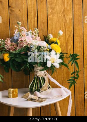 Bouquet di fiori legati con un nastro si erge su una sedia contro una parete di legno Foto Stock