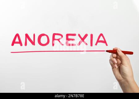 Donna che scrive parola ANORESSIA su vetro su sfondo bianco, primo piano Foto Stock