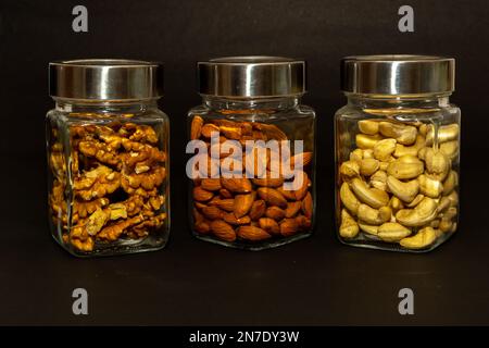 Vasetti di vetro riempiti con varietà di frutta secca su fondo nero Foto Stock