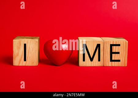 Frase Io mi amo fatto con cubi di legno e cuore su sfondo rosso Foto Stock