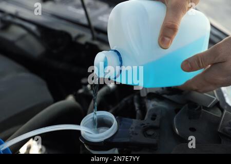 Man che versa l'antigelo dal contenitore in plastica nel serbatoio del liquido lavacristalli, fare un primo piano Foto Stock