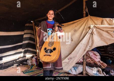 Una ragazza beduina posa con una chitarra per essere fotografata in una tenda nomade nel panoramico sito patrimonio dell'umanità dell'UNESCO del deserto di Wadi Rum. Il Wadi Rum è acclamato come una delle regioni più panoramiche del mondo. Foto Stock