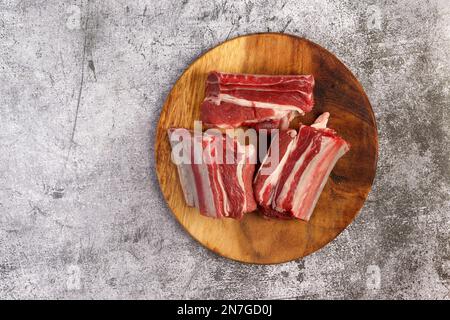 Costolette di manzo crudo su un asse di legno da taglio su sfondo grigio scuro. Vista dall'alto, disposizione piatta Foto Stock