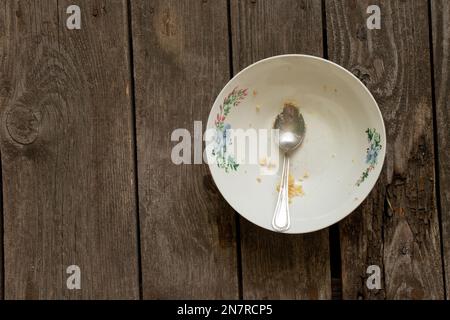 piatto sporco dopo il pasto con un cucchiaio su un tavolo di legno Foto Stock