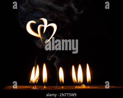 candele, fumo e due cuori formati dal fuoco di candele, su uno sfondo nero Foto Stock