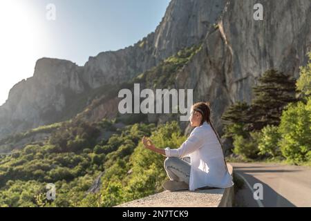 Profilo di una donna che fa yoga in cima a una scogliera in montagna. Donna medita nello yoga asana Padmasana. Foto Stock